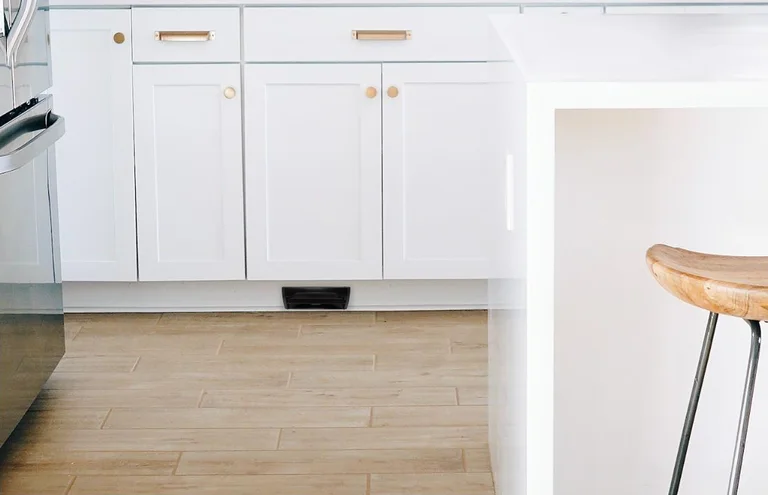 A VacPort set into a kitchen toe kick under white cabinets
