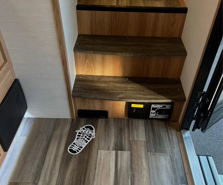 A VacPort installed in a toe kick at the base of a set of stairs, with a footprint marking where to sweep
